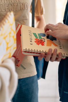 a person holding a book in their hand and another person standing next to it with other people behind them