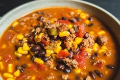 a white bowl filled with chili and ground beef soup on top of a wooden table