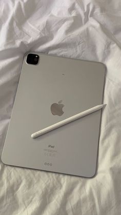 an ipad with a pencil on top of it sitting on a white sheet covered bed