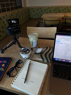 an open laptop computer sitting on top of a wooden table next to a notebook and camera