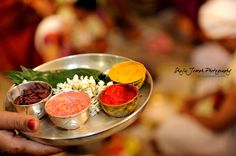 a person holding a metal plate with different colored powders and spices on it in front of other people