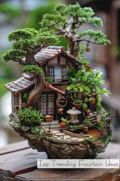 a miniature house made out of rocks with trees and plants on the roof, sitting on top of a wooden table