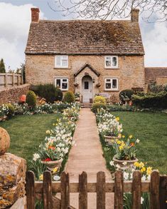 a brick house with flowers in the front yard and a wooden fence around it on a sunny day