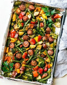 a sheet pan filled with sausage and veggies on top of a white table