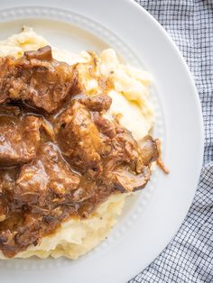 meat and gravy on mashed potatoes on a white plate with a blue checkered cloth