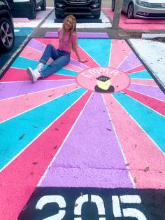 a woman sitting on the ground in front of a parking lot painted with colorful paint