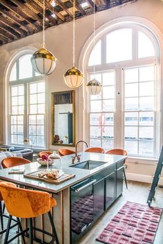 a kitchen with an island and lots of chairs around it in front of two large windows