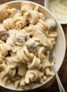 a white bowl filled with pasta covered in mushrooms and sauce next to a small bowl of grated cheese