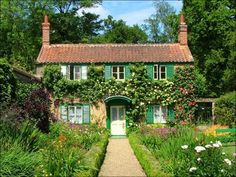 an old house with green shutters and flowers around it