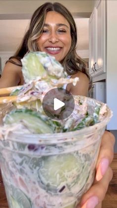 a woman holding up a plastic cup filled with food and vegetables in it's hands