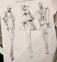 three sketches of women's fashions on paper with pen and scissors next to them