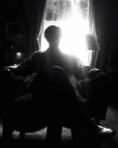 a man sitting on top of a couch next to a window in a dark room