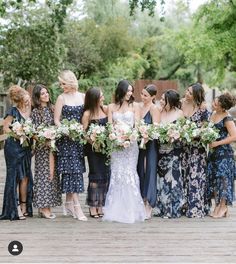 a group of women standing next to each other on a wooden bridge holding bouquets