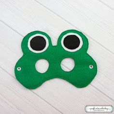 a green felt mask with eyes and nose on a white wooden surface, ready to be made into a costume