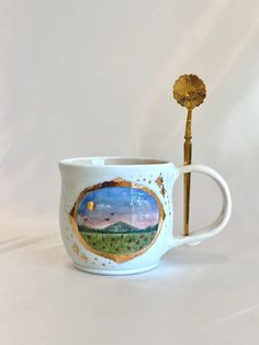 a coffee cup with a golden flower on the top and an image of a landscape painted on it