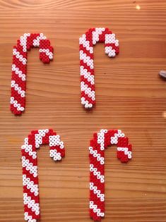 four candy canes made out of perler beads on a wooden surface with the letters p, t, and f