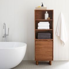 a white bath tub sitting next to a wooden shelf filled with folded towels and blankets