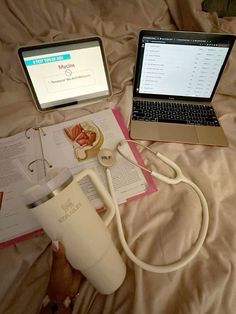 an open laptop computer sitting on top of a bed next to a cup and book