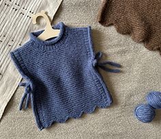 a blue knitted sweater next to skeins of yarn