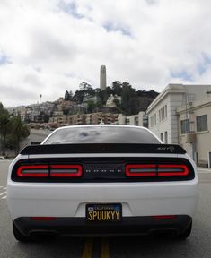 the rear end of a white sports car parked in a parking lot next to some buildings