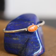 At LBJ this is called the Simple Cuff Bracelet - which is true. But when you're working with the wonderful stones we are -- like the gorgeous, soft salmony orange red Spiny Oyster Shell in this Orange/Red Spiny Oyster Bracelet -- you don't need much embellishment besides the gorgeous, Spiny Oyster in minimal .925 Sterling Silver Setting. Here we've used a low-dome half-round wire and two sterling silver bead embellishments to flank this 8X14mm spiny oyster oval. Wear alone or stack 'em up! All t Sterling Silver Bangle Bracelet With Natural Stones, Oval Cuff Bracelet With Polished Finish As Gift, Sterling Silver Gemstone Bangle, Oval Stackable Bracelets As Gift, Oval Stackable Bracelets For Gifts, Stackable Oval Bracelets As Gift, Oval Stackable Bracelets For Gift, Spiritual Polished Bangle Bracelet, Oval Sterling Silver Bangle As Gift