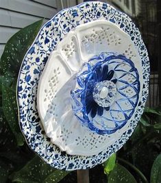 a decorative blue and white flower on top of a wooden stick in front of a house