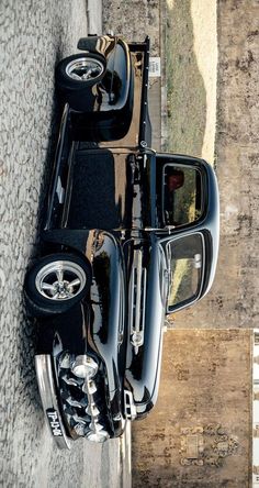 a black car parked on the side of a road next to a stone wall and sidewalk