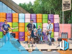 a group of men standing on top of a wooden platform next to colorful barrels with guitars