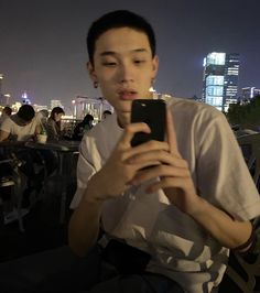 a man sitting on a bench looking at his cell phone in front of the city skyline