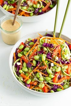 a salad with carrots, edama and sprouts in a white bowl