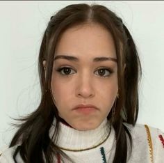 a woman with long hair wearing a white sweater and gold hoop earrings is looking at the camera