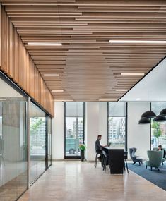 an office with large windows and wooden slats on the ceiling, along with people sitting at desks