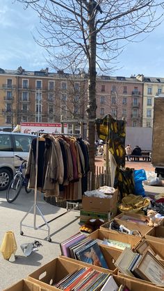 an outdoor clothing stand with clothes on display and parked cars in the back ground behind it