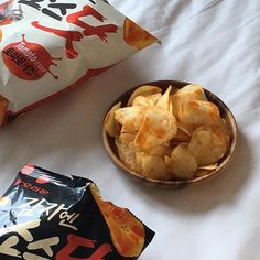 chips in a wooden bowl next to a bag of cheetos on a bed