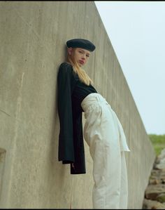 a woman leaning up against a wall wearing a black hat