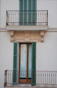 an open window with green shutters on a white wall and balconies in front of it