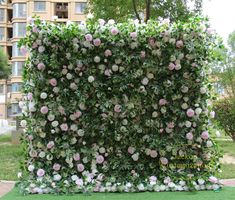 an artificial garden wall with pink and white flowers in the center, surrounded by green grass