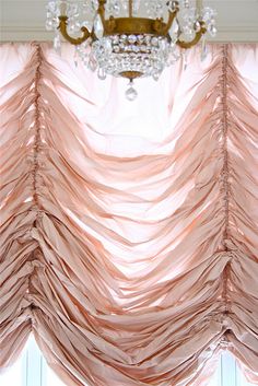 a chandelier hanging from the ceiling in front of a curtain with feathers on it