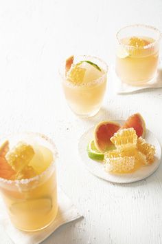 three glasses filled with different kinds of fruit on top of a white tablecloth next to two small plates