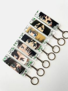 five anime key chains with eyes and green leaves hanging from them on a white surface