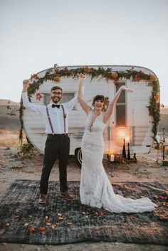 a newly married couple standing in front of a trailer with their arms up and smiling at the camera