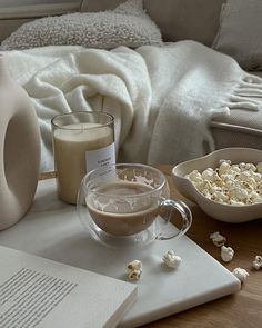 a table topped with a book, bowl of popcorn and a cup of coffee next to a bottle of milk