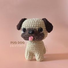 a small crocheted pug dog sitting on top of a pink surface with its tongue out