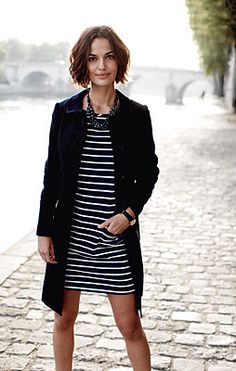 a woman standing on a cobblestone road wearing a black coat and striped dress