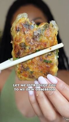 a woman holding up a piece of food with chopsticks