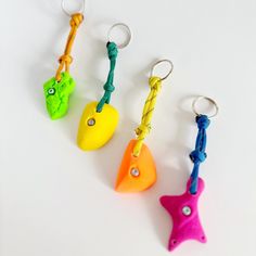 four different colored plastic objects are hanging from hooks on a white surface, one is shaped like a starfish and the other has a rope attached to it's end