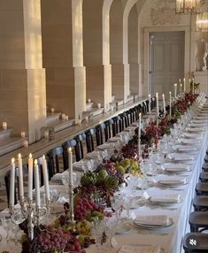 the long table is set with many plates and glasses, candles, and fruit on it