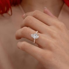 a woman's hand with a diamond ring on her left hand and red hair in the background