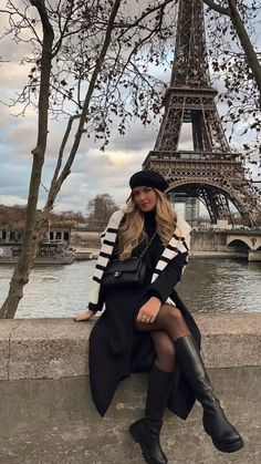 a woman is sitting on the wall in front of the eiffel tower with her legs crossed