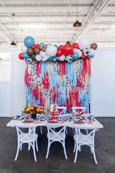 a party table with balloons and streamers on the wall in front of it is set up for an event